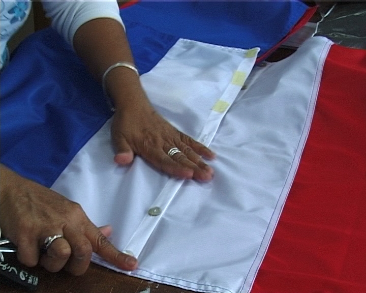 photo extraite d'une video, des mains boutonnent le drapeau tricolore